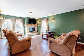 Ein Wohnzimmer mit zwei Liegesofas, einem Kamin aus Stein, einem Flachbildfernseher und einem kleinen runden Tisch mit einer Vase.