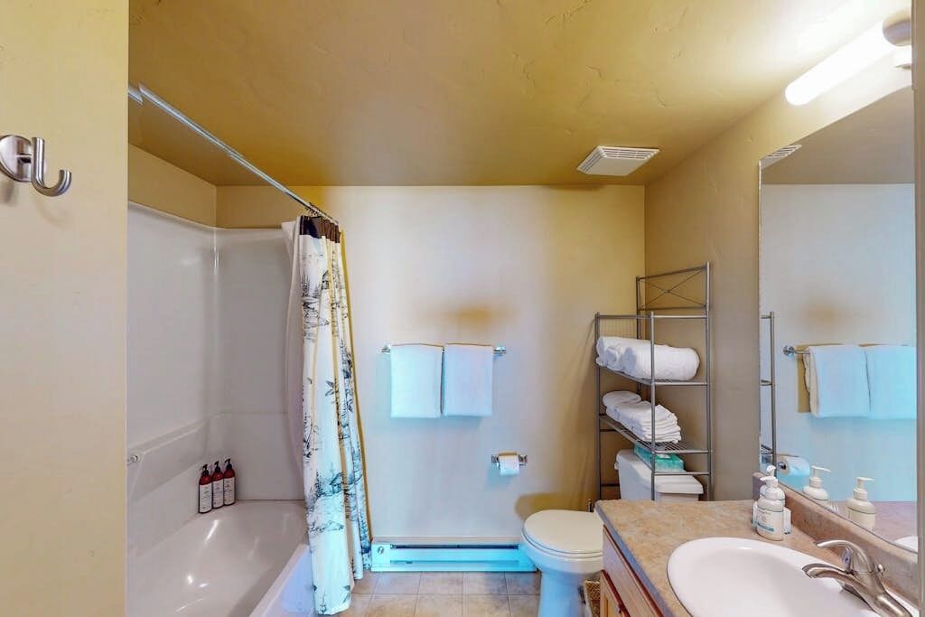A bathroom with a bathtub, toilet, and sink, with towels and toiletries on shelves.