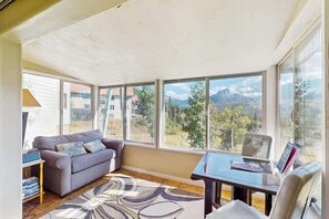 Ein sonnendurchfluteter Raum mit einer Couch, einem Tisch und großen Fenstern mit Blick auf die Berge.