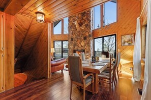 Ein Holzinnenraum mit Kamin aus Stein, einem Esstisch und einem großen Fenster.
