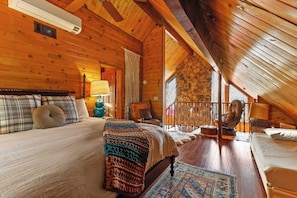 Ein gemütliches Schlafzimmer in einer Blockhütte mit Bett, Sessel, Lampe und einer Steinwand.