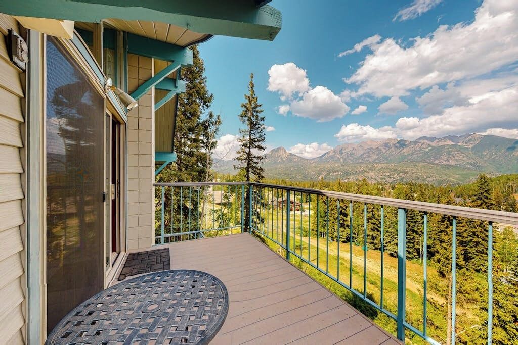 A balcony with a view of mountains, a table, and a railing.