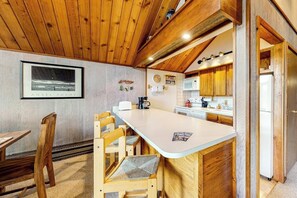 A kitchen with wooden cabinets, a white countertop, and a dining area with wooden chairs. - Ski-in/ski-out gem - top-floor condo - lake & mountain views, fireplace (Durango)