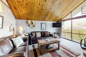 A living room with a wooden ceiling, leather sofa, a coffee table, and a large window with a view of trees. - Ski-in/ski-out gem - top-floor condo - lake & mountain views, fireplace (Durango)