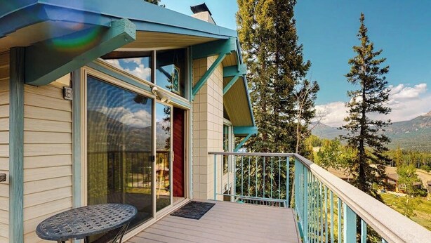 Una terraza de madera con una mesa, un vidrio y vistas a árboles y montañas.