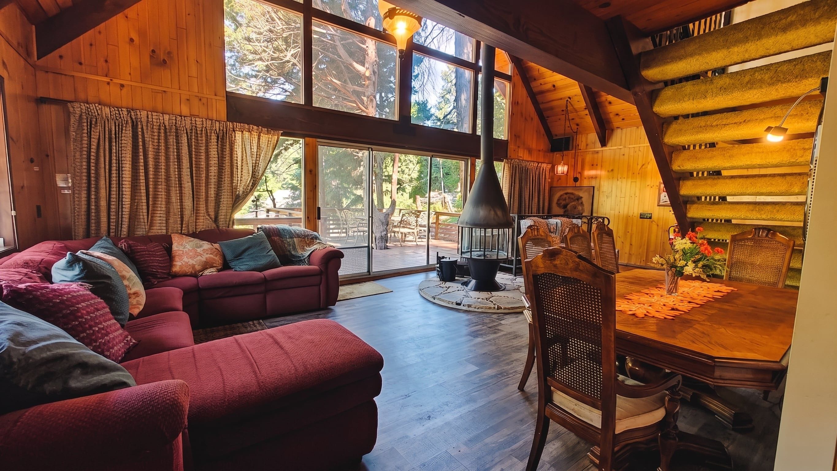 L’intérieur chaleureux d’un chalet avec un grand plafond en bois, une cheminée, une table à manger avec des chaises et un canapé agrémenté de coussins.