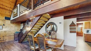 A wooden interior with a dining table, chairs, a staircase, and a kitchen area. - Rustic, wooded escape near the village w/ a lovely deck (Lake Arrowhead)