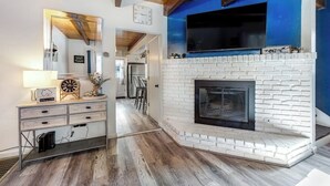 A living room with a white brick fireplace, a mounted TV, and a wooden ceiling. - Dog-friendly retreat with fast WiFi, washer/dryer & wood-burning fireplace (Running Springs)