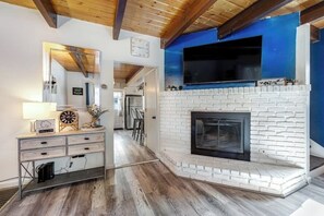 A living room with a white brick fireplace, a mounted TV, and a wooden ceiling. - Dog-friendly retreat with fast WiFi, washer/dryer & wood-burning fireplace (Running Springs)