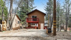 A two-story wooden cabin with a red balcony, surrounded by trees. - Dog-friendly retreat with fast WiFi, washer/dryer & wood-burning fireplace (Running Springs)