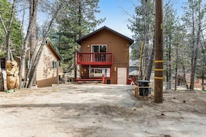 A two-story wooden cabin with a red balcony, surrounded by trees. - Dog-friendly retreat with fast WiFi, washer/dryer & wood-burning fireplace (Running Springs)