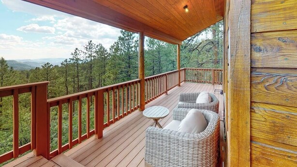 Un terrazzo in legno con mobili in vimini e vista su un paesaggio boschivo.