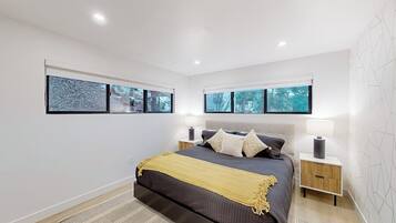A modern bedroom with a large bed, two bedside tables, and a view of trees through the windows.