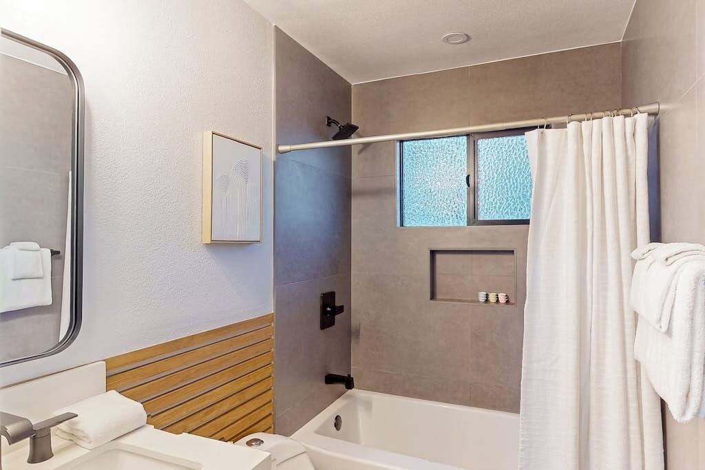 A modern bathroom with a bathtub, a shower area, a mirror, and a window.