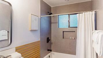 A modern bathroom with a bathtub, a shower area, a mirror, and a window.