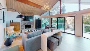 A modern living room with a fireplace, large windows, and a high ceiling. - Dog-friendly home with beautiful views, large deck, smart TVs & lake access (Lake Arrowhead)