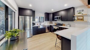 A modern kitchen with dark cabinets, stainless steel appliances, and a large window. - Dog-friendly home with beautiful views, large deck, smart TVs & lake access (Lake Arrowhead)