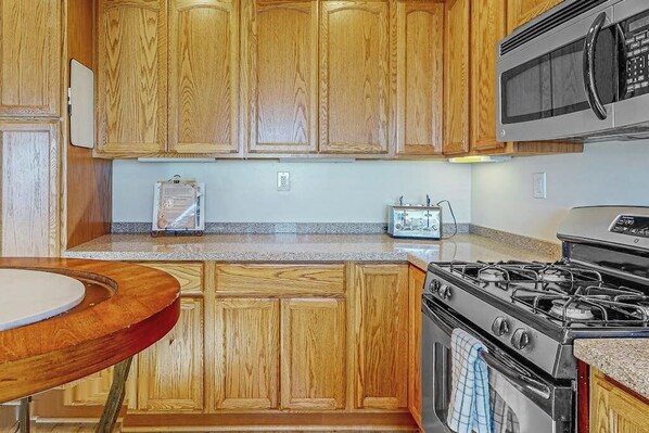 A kitchen with wooden cabinets, a microwave, a stove, and a small table. - SkyPark cabin w/incredible views - close to Santa (Skyforest)