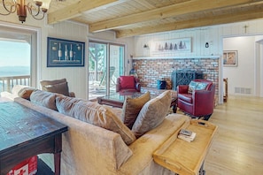 Ein gemütliches Wohnzimmer mit einer Couch, Sesseln, einem Kamin und Blick durch ein großes Fenster.