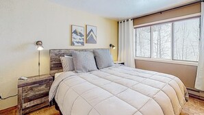 Un dormitorio con cama, mesitas de noche, lámpara y ventana con vistas.