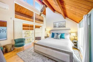 Ein Schlafzimmer mit einem großen Bett, Holzbalkendecke, einem Balkon und Blick auf Bäume.