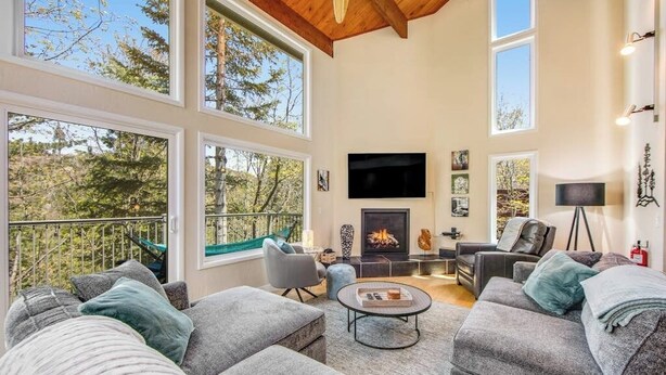 A spacious living room with large windows, a fireplace, and modern furniture. - Modern alpine escape with two decks, grill, private sauna, fireplace (Lake Arrowhead)
