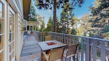 Un espace extérieur abrité, doté d’une table et de chaises, entouré d’une rambarde en bois et offrant une vue sur un paysage boisé.