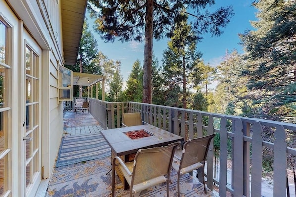 Ein überdachter Außenbereich mit Tisch und Stühlen, umgeben von einem Holzbalkon, mit Blick auf eine bewaldete Landschaft.