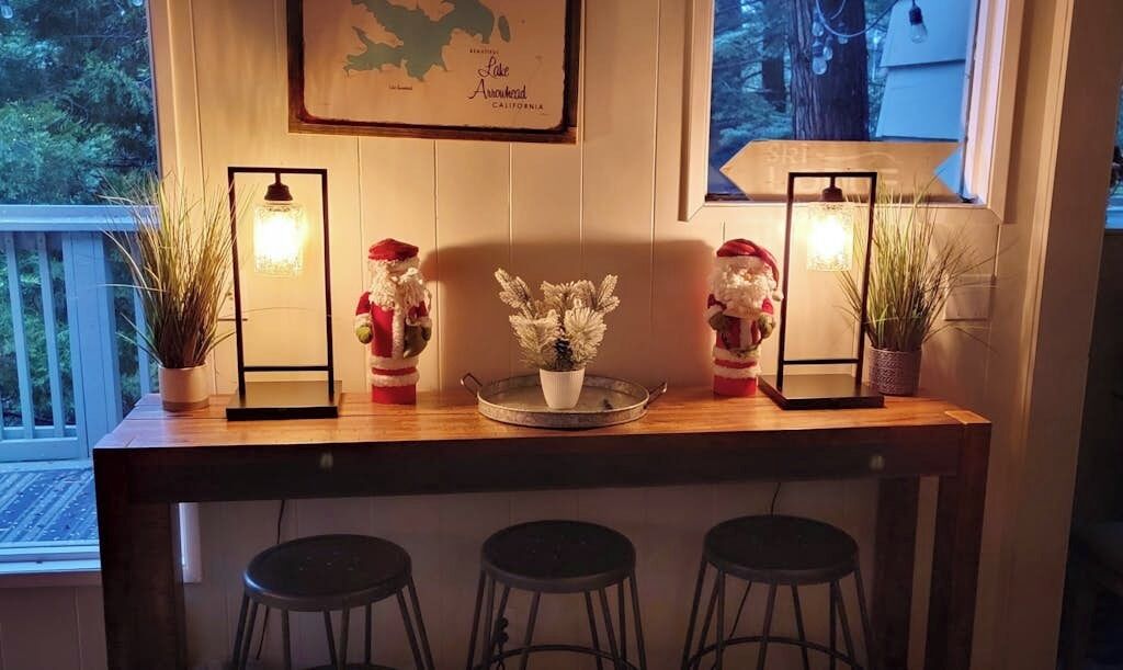 Un comptoir de bar en bois, agrémenté de deux plantes en pot, d’un élément décoratif central et de deux lampes fixées au mur.