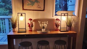 A wooden bar counter with two potted plants, a decorative centerpiece, and two wall-mounted lights. - Tree-surrounded retreat w/ balcony, patio, fireplace, Lake access, washer/dryer (Lake Arrowhead)
