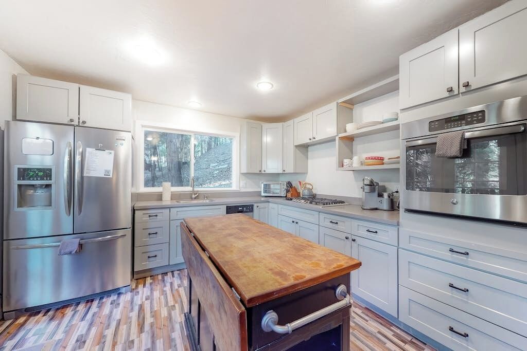 A modern kitchen with stainless steel appliances, light-colored cabinetry, and a wooden island.