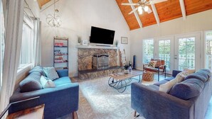 A spacious living room with a stone fireplace, a television mounted above it, and a ceiling fan. - Tree-surrounded retreat w/ balcony, patio, fireplace, Lake access, washer/dryer (Lake Arrowhead)