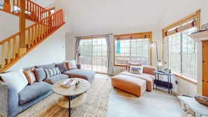 A spacious living room with a staircase, large windows, and a cozy seating area. - Spacious home with three decks, views, game room, fireplace, & fast WiFi (Lake Arrowhead)