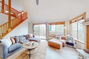 A spacious living room with a staircase, large windows, and a cozy seating area. - Spacious home with three decks, views, game room, fireplace, & fast WiFi (Lake Arrowhead)