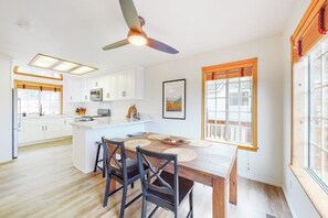 A modern kitchen with white cabinets, a central island, and a dining area with a wooden table and chairs. - Spacious home with three decks, views, game room, fireplace, & fast WiFi (Lake Arrowhead)