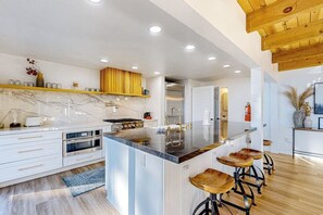 Eine moderne Küche mit Marmorarbeitsplatte, Edelstahlgeräten, Holzstühlen und Holzboden.