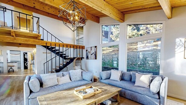 Uma sala de estar ampla com teto de madeira, uma janela grande, uma escada e um sofá modular.