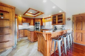 Eine Küche mit Holzschränken, einer zentralen Kochinsel inklusive Sitzgelegenheiten, einer Mikrowelle und einem Kühlschrank.