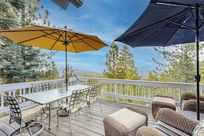 Eine Holzterrasse mit Tisch und Stühlen, zwei Sonnenschirmen, Korbmöbeln und einem weißen Geländer.