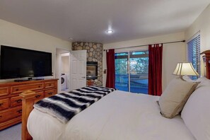 Ein Schlafzimmer mit Bett, Fernseher, Kommode, einer Steinwand, einer Glastür und einem Balkon.