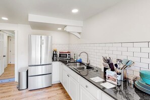 Eine moderne Küche mit weißen Schränken, Edelstahlgeräten, einer schwarzen Arbeitsplatte und einer gefliesten Rückwand.