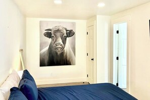 Ein Schlafzimmer mit einem Bett, einem an der Wand hängenden Gemälde einer Kuh und einer weißen Tür.