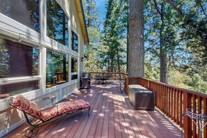 Eine Holzterrasse mit einer Bank, einem Tisch und Grillplatz, umgeben von hohen Bäumen.