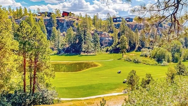Ein Golfplatz mit Teich, umgeben von Bäumen und einer steilen Felswand.