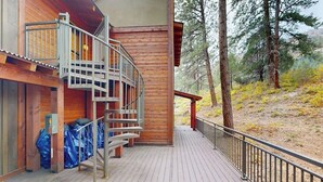 Eine Holzhütte mit einer Holzdiele, einer Metalltreppe und Blick auf ein bewaldetes Gebiet.
