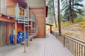 Eine Holzhütte mit einer Holzdiele, einer Metalltreppe und Blick auf ein bewaldetes Gebiet.