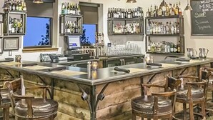Eine Bar mit Holzhockern, einer Theke und Regalen voller Flaschen.