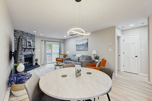 Ein modernes Wohnzimmer mit Kamin, rundem Esstisch und bequemen Sitzgelegenheiten.