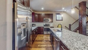Une cuisine équipée d’appareils électroménagers en acier inoxydable, de meubles de rangement en bois foncé, d’un plan de travail en granit et d’un parquet.