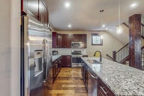 A kitchen with stainless steel appliances, dark wood cabinets, a granite countertop, and a wooden floor. - Beautiful townhome w/ balcony, hot tub & mountain views. Close to slopes (Keystone)